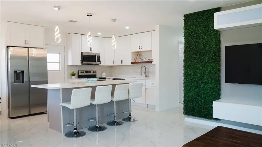 Two tone kitchen with stainless steel appliances, pendant lighting, a kitchen island, a breakfast bar area, and open shelves