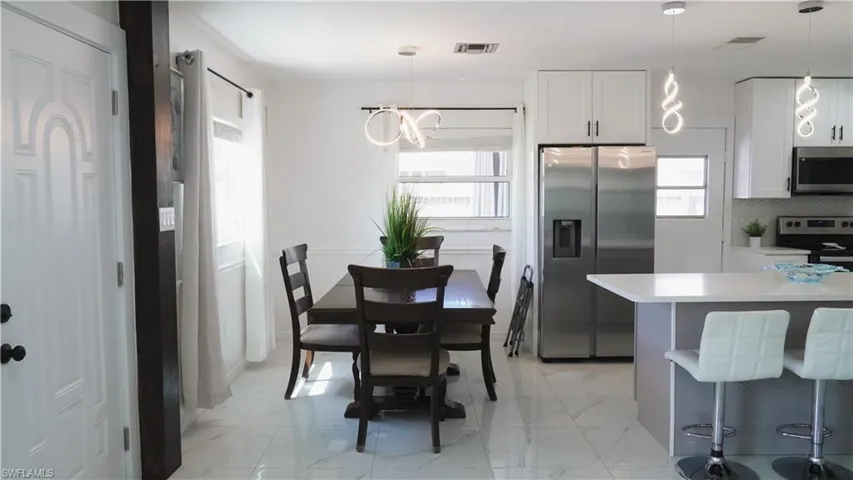 Kitchen featuring stainless steel appliances, a kitchen bar, white cabinets, hanging light fixtures, and light marble finish flooring