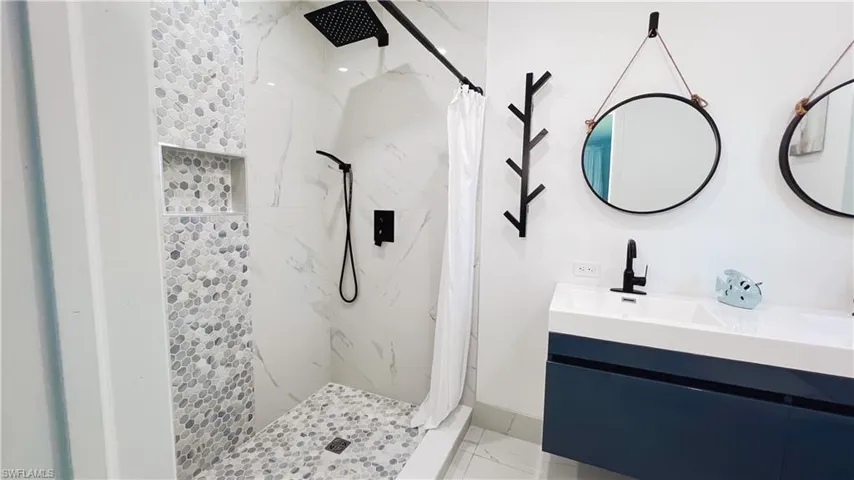 Bathroom with a marble finish shower, vanity, and light marble finish floors