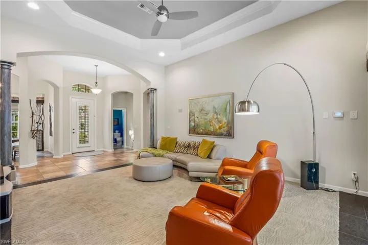 living room featuring ceiling fan, crown molding, a tray ceiling, and ornate columns