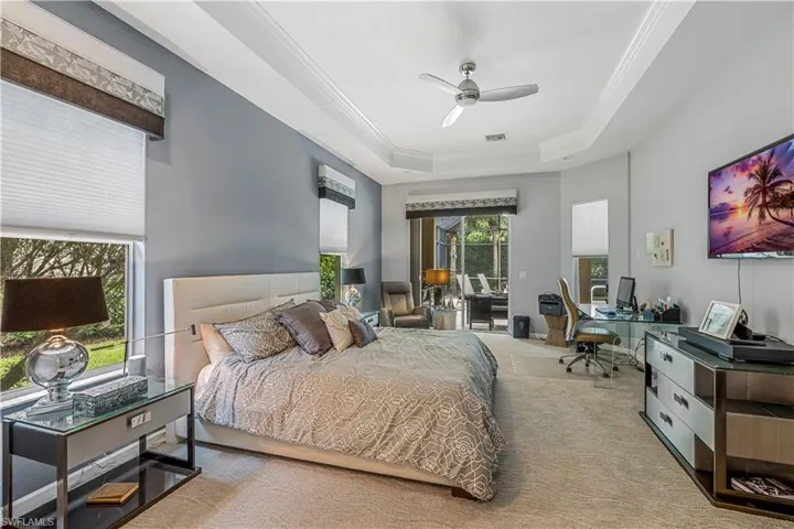Carpeted bedroom with a raised ceiling, ornamental molding, and ceiling fan