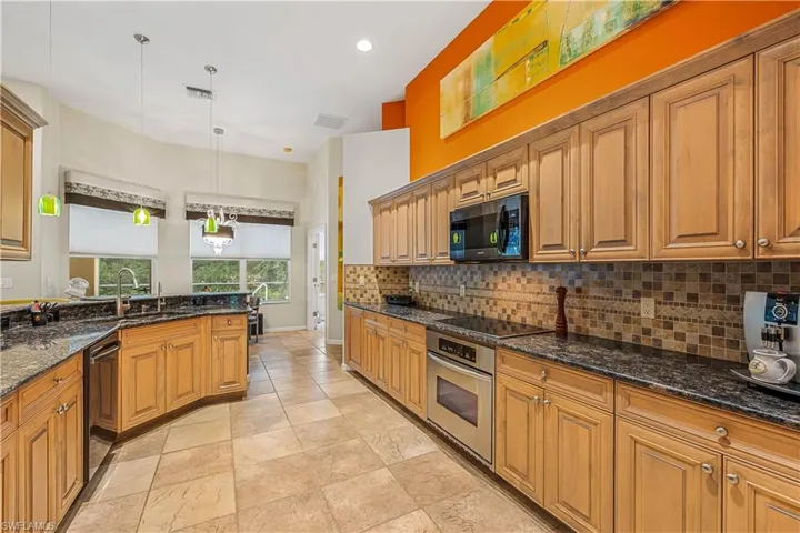 Kitchen granite counters, stainless appliances, pendant lighting, decorative tile backsplash, and sink