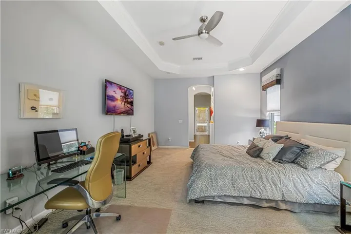 Bedroom with ensuite bath, carpet, ceiling fan, a raised ceiling, and ornamental molding