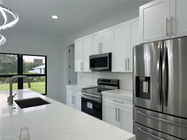 Kitchen with stainless steel appliances, white cabinets, light stone counters, recessed lighting, and pendant lighting
