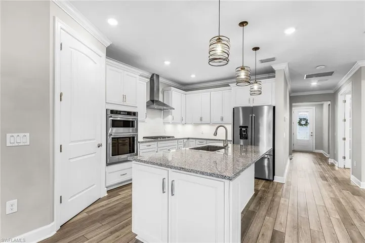 Kitchen with backsplash, light stone counters, ornamental molding, white cabinetry, and stainless steel appliances
