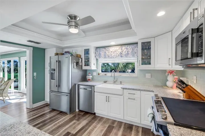 Kitchen featuring a raised ceiling, white cabinetry, light stone countertops, and recessed lighting