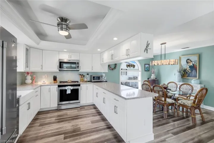 Kitchen featuring backsplash, light stone counters, a raised ceiling, ornamental molding, and appliances with stainless steel finishes