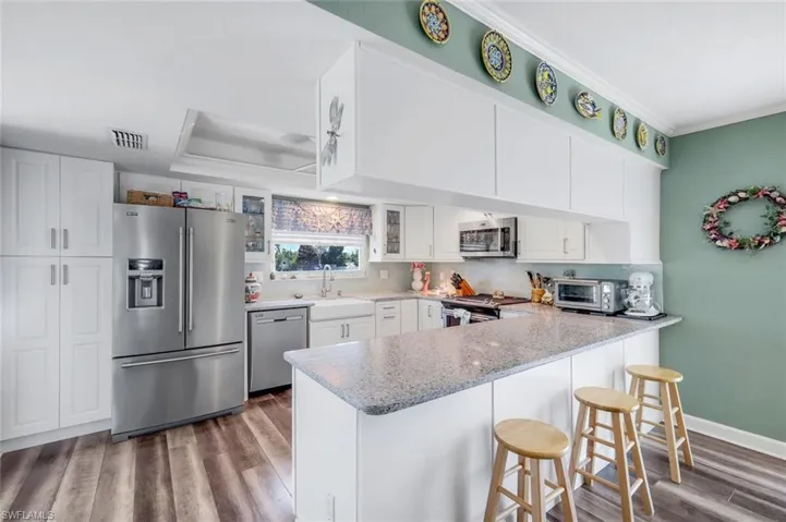 Kitchen featuring stainless steel appliances, dark wood-style flooring, white cabinets, a breakfast bar area, and a peninsula
