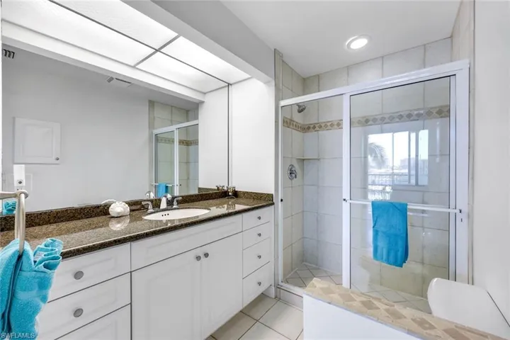 Primary bathroom with tiled, walk-in shower & granite countertop on spacious vanity.