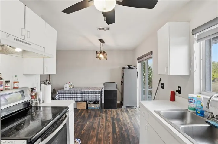 Kitchen featuring stainless steel appliances, white cabinets, under cabinet range hood, light countertops, and dark wood-style floors