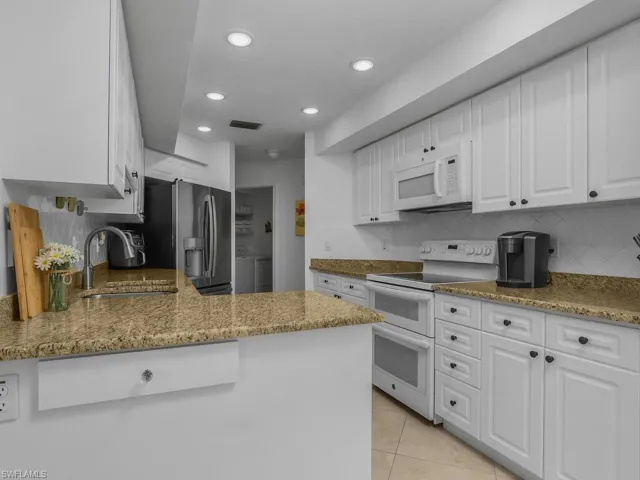 Kitchen with white cabinetry, appliances, granite counters, a peninsula, and recessed lighting