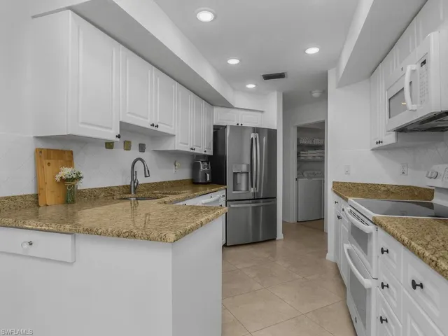 Kitchen with appliances, granite countertops, white cabinetry, backsplash, and recessed lighting
