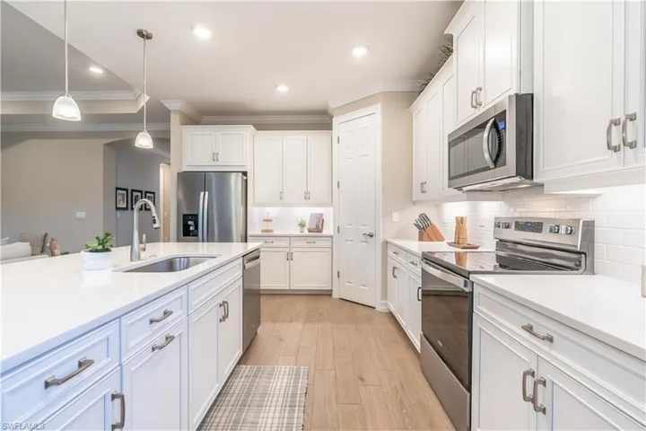 Kitchen featuring hanging light fixtures, sink, white cabinetry, appliances with stainless steel finishes, and light hardwood / wood-style floors