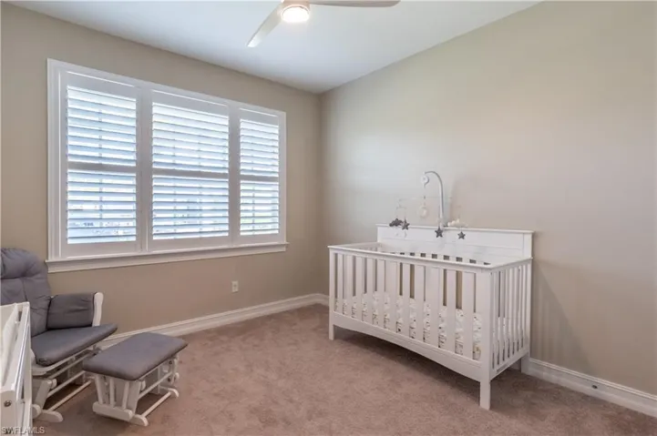 Carpeted bedroom featuring a crib and ceiling fan