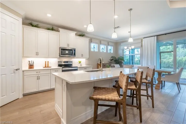 Kitchen featuring appliances with stainless steel finishes, decorative light fixtures, and white cabinets