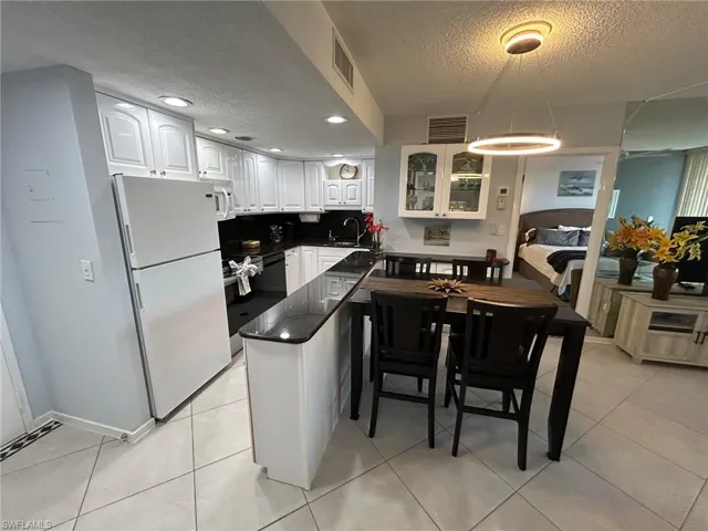 Kitchen with white cabinets, white appliances, a textured ceiling, a peninsula, and decorative light fixtures