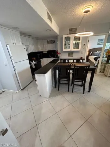Kitchen with white cabinetry, dark countertops, fridge, a textured ceiling, and light tile patterned floors