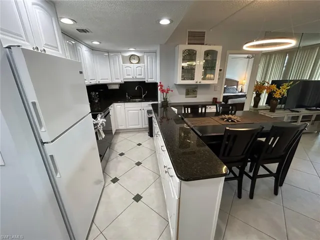 Kitchen with freestanding refrigerator, white cabinetry, a textured ceiling, light tile patterned floors, and glass insert cabinets