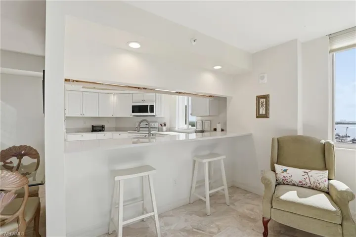 Kitchen featuring white cabinets, a kitchen breakfast bar, white appliances, a peninsula, and recessed lighting - Virtually Edited Image