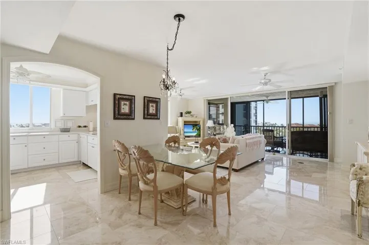 Dining area with ceiling fan, light marble finish flooring, a chandelier, healthy amount of natural light, and expansive windows - Virtually Edited Image