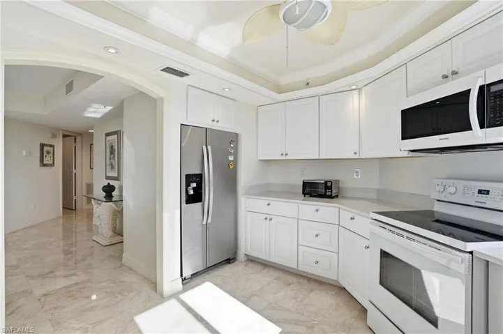 Kitchen featuring white appliances, a tray ceiling, ornamental molding, arched walkways, and light countertops - Virtually Edited Image