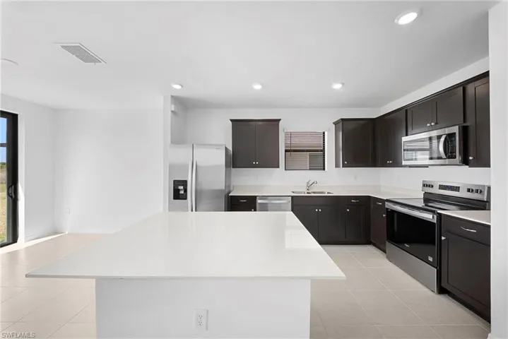 Kitchen featuring stainless steel appliances, a kitchen island, recessed lighting, light tile patterned floors, and light stone countertops
