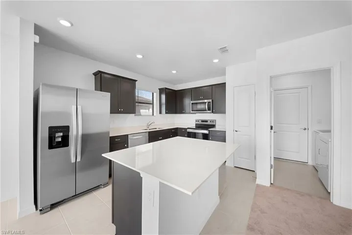 Kitchen with stainless steel appliances, a center island, light tile patterned flooring, washer and dryer, and dark wood finish cabinetry
