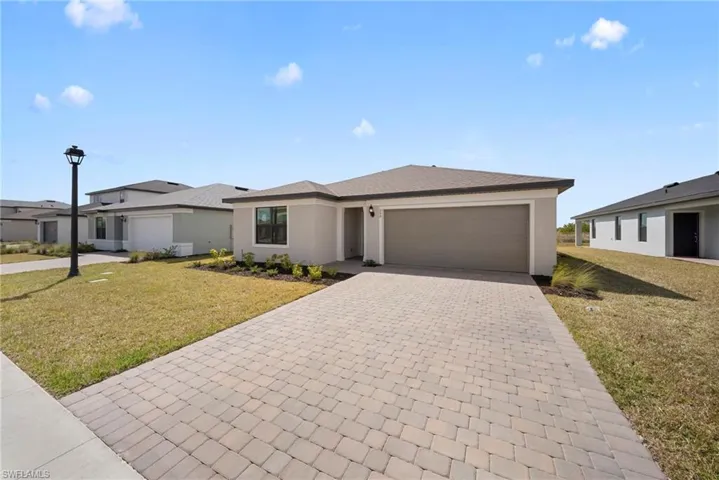 Prairie-style home featuring a front yard, decorative driveway, a garage, and stucco siding