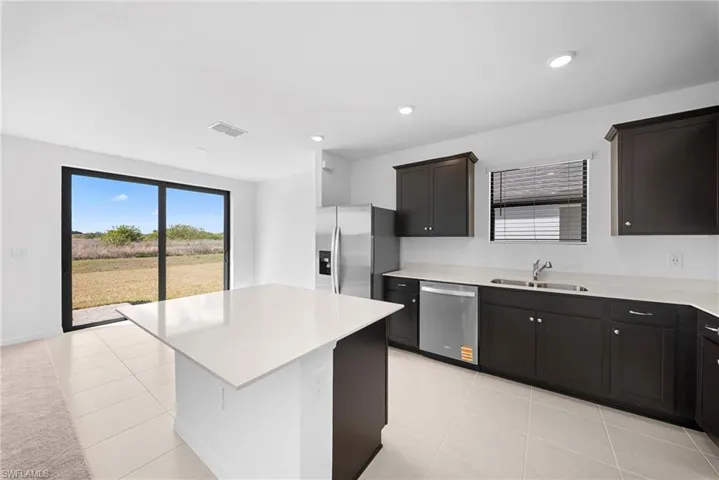Kitchen featuring stainless steel appliances, light tile patterned flooring, a center island, dark wood finish cabinets, and recessed lighting