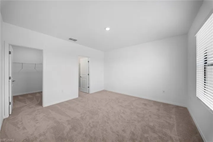 Unfurnished bedroom with a walk in closet and light colored carpet