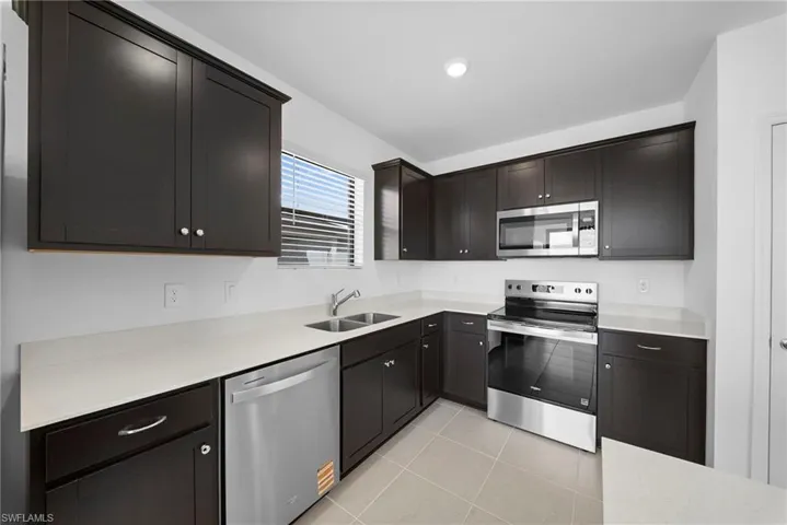 Kitchen featuring stainless steel appliances, light tile patterned floors, and dark wood finish cabinets
