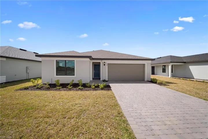 View of front of house with stucco siding, decorative driveway, and a front yard