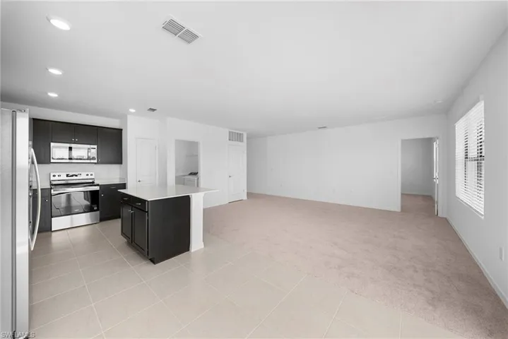 Kitchen with light carpet, stainless steel appliances, a kitchen island, dark cabinets, and light tile patterned flooring