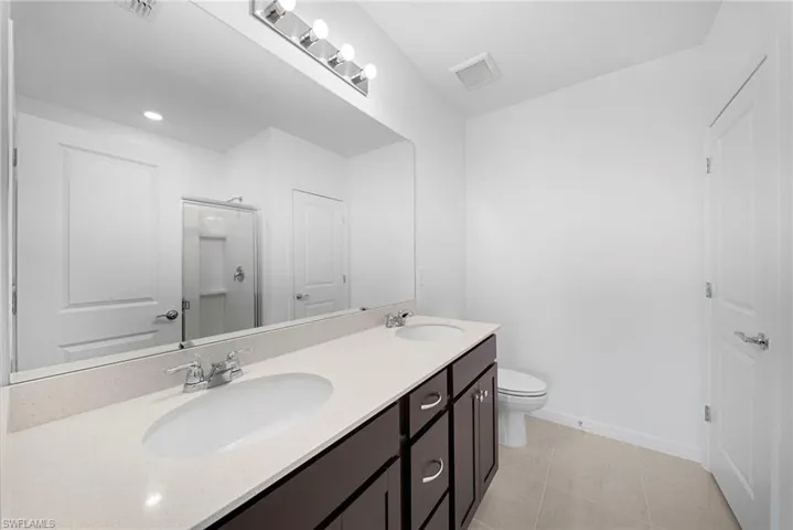 Full bath featuring a shower stall, double vanity, and light tile patterned flooring