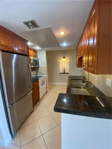 Kitchen featuring light tile patterned floors, dark stone counters, range, refrigerator, and sink