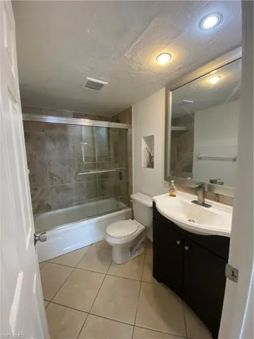 Full bathroom with toilet, tile patterned flooring, vanity, a textured ceiling, and shower / bath combination with glass door