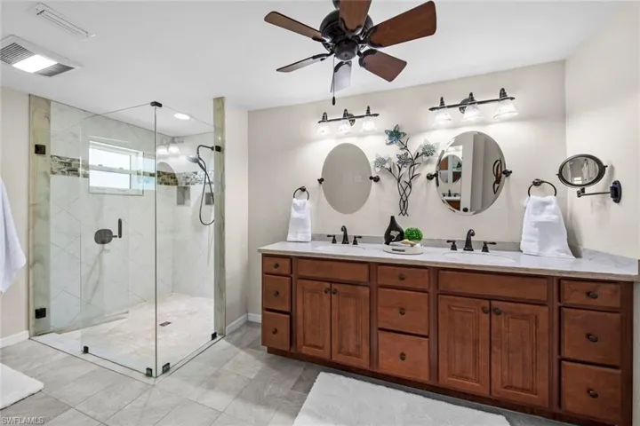 Primary updated bathroom with dual sinks and walk in seamless glass shower