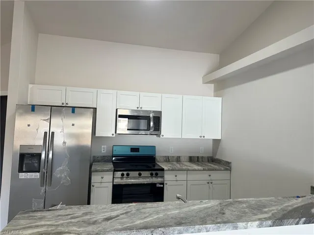 Kitchen with stainless steel appliances, white cabinets, and light stone counters