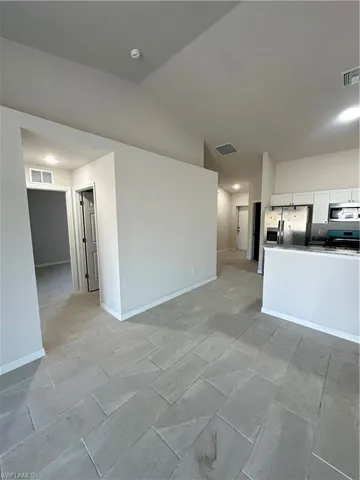 Unfurnished living room featuring lofted ceiling and baseboards