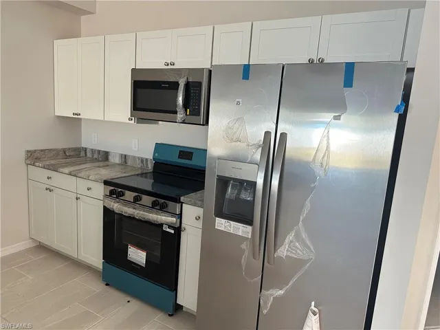 Kitchen with stainless steel appliances, white cabinetry, and dark stone counters