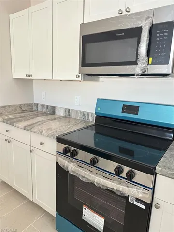 Kitchen featuring stainless steel appliances, white cabinetry, and light stone countertops