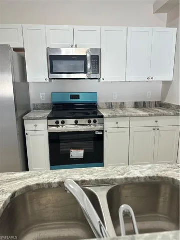 Kitchen with stainless steel appliances, white cabinets, and light stone countertops