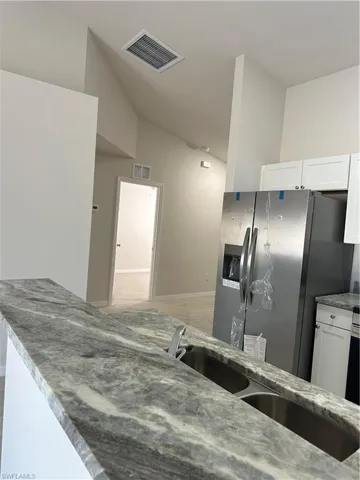 Kitchen featuring white cabinets, light stone counters, stainless steel refrigerator, and vaulted ceiling