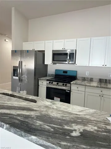 Kitchen with light stone counters, white cabinets, and stainless steel appliances