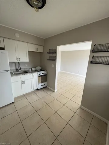 Kitchen with white appliances, a sink, white cabinets, light tile patterned floors, and a textured ceiling
