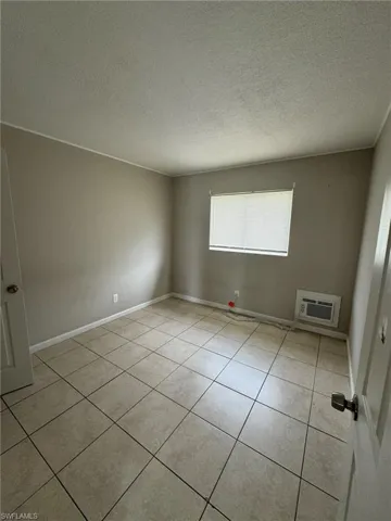 Empty room featuring an AC wall unit, light tile patterned floors, a textured ceiling, and baseboards
