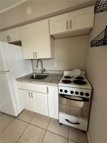 Kitchen featuring white appliances, a sink, light tile patterned floors, white cabinets, and light stone countertops