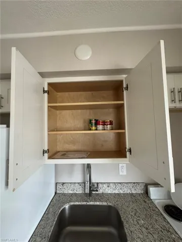 Kitchen view of a sink, light stone counters, white cabinets, and a textured ceiling