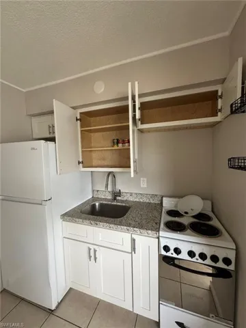 Kitchen featuring a sink, open shelves, white appliances, light tile patterned floors, and stone counters