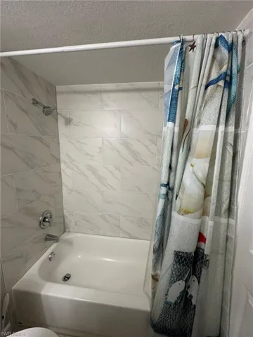 Full bathroom featuring shower / bathtub combination with curtain and a textured ceiling